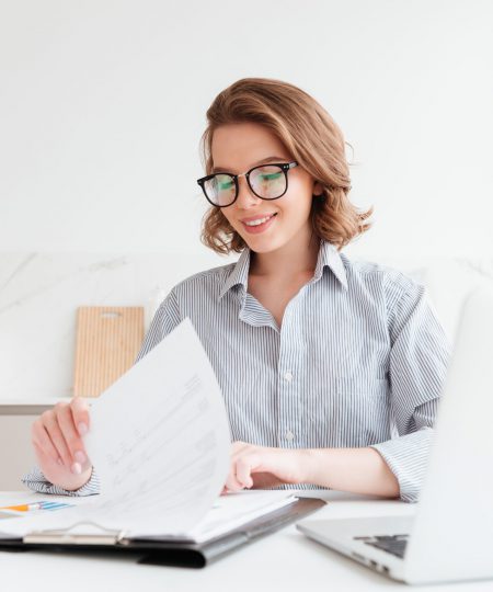 Photo of cheerful attractive woman in glasses reading new contract while working in the kitchen